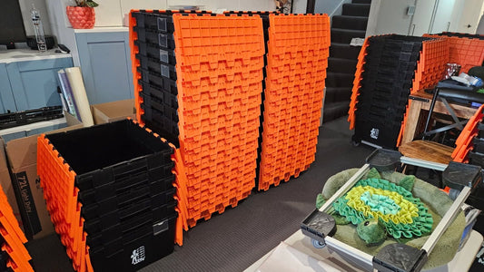 Tall stacks of orange and black Move Mate crates in a room with a table nearby